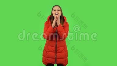 可爱的女孩穿着一件红色羽绒服，拍手，带来了喜悦和喜悦。 绿色屏幕
