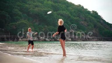 一个阳光明媚的日子，两个年轻的女人在热带海滩扔<strong>飞盘</strong>。