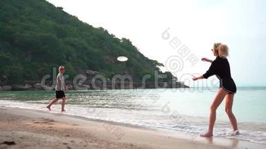 一个阳光明媚的日子，两个年轻的女人在热带海滩扔<strong>飞盘</strong>。