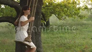 自由女孩在阳光下在橡树枝上荡秋千。 飞行的梦想。 快乐的童年概念。 一个漂亮的女孩