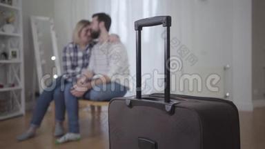 站在前台的手提箱的特写镜头，就像幸福的年轻夫妇在后台拥抱一样。 已婚男女