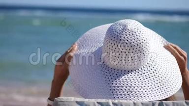 特写镜头。 模糊的水背景。 戴着白色大帽子的年轻女人坐在海边，戴着她的帽子。 有文字的地方