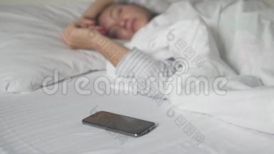 一个女人早上在床上关掉手机上的闹钟。 在电话的焦点上
