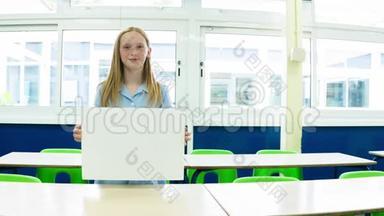 白人小学女孩在教室里举着一张空白的标语牌