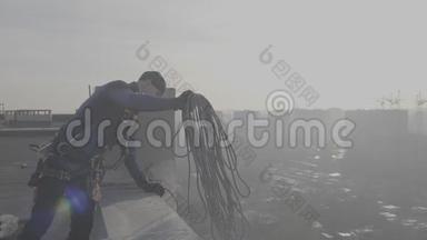 穿着特殊制服的男登山者站在屋顶上，扔下一根电缆，他将从外面下去