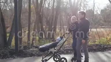 幸福的年轻家庭在公园里溜冰。 爸爸妈妈正在和婴儿车里的一个婴儿轮滑。 安全