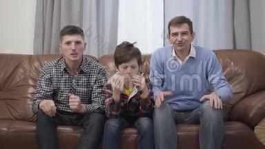 三个不同年龄的男人在电视上看足球比赛和打手势的肖像。 可悲的白人儿子，父亲和