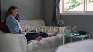 一个年轻的女人拿着笔记本电脑坐在沙发上打视频电话。