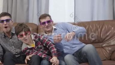 三个不同年龄的白人男子坐在家里的沙发上，戴着3D护目镜看电视。快乐的多代人