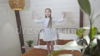 一幅快乐的小白种人女孩在家玩得开心的肖像。 欢乐的孩子在室内的床上跳舞和跳跃