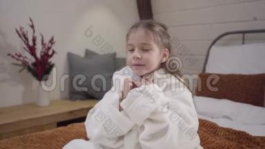 镜头接近迷人的白种人女孩，美丽的眼睛坐在床上，穿着白色的浴袍。 肖像