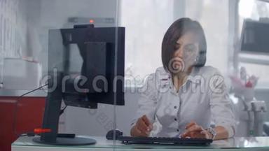 一位穿着白色外套的女医生看着坐在玻璃墙<strong>后面</strong>明亮办公室里的监视器屏幕。 现代诊所