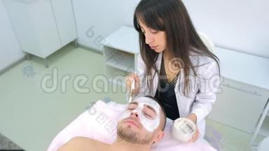 美容师正在用刷子`人脸上涂白色<strong>保湿面膜</strong>。