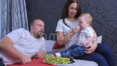 一家人的妈妈、爸爸和小女孩正在家里一起在床上吃葡萄。