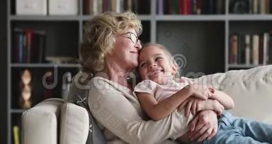 快乐轻松的老奶奶拥抱学龄前孙女休息沙发