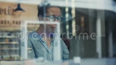 一个戴眼镜的女人用手提电脑通过玻璃拍摄