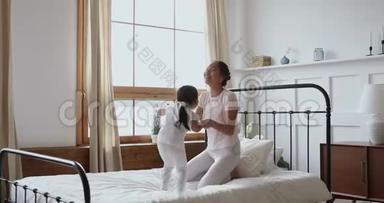 无忧无虑的亚洲小女儿在床上蹦蹦跳跳地和妈妈玩耍