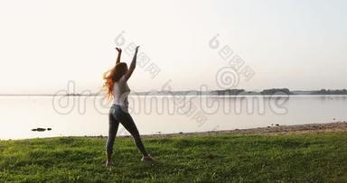 年轻运动的女人，留着<strong>长长</strong>的卷曲的红色头发，在湖岸上做活动。