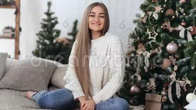 微笑的<strong>家庭妇女</strong>摆在舒适的沙发上与圣诞树。 4k龙红相机