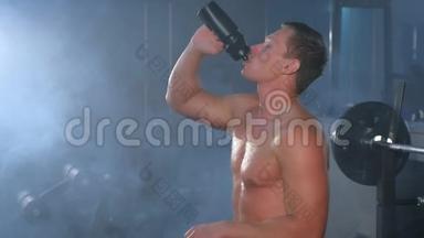 肖像肌肉运动员健美运动员在健身房里从瓶子里喝水。