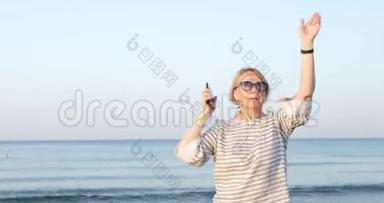戴墨镜的金发老妇人正在沙滩上跳舞。