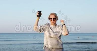 戴墨镜的金发老妇人正在海边散步和滑稽的舞蹈。