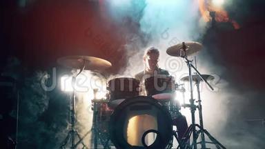 音乐家正在乌云密布的录音室里演奏架子鼓. 男鼓手在烟雾中打鼓。