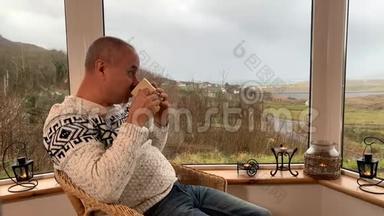 男人坐在阳台上舒适的柳条椅子上，喝着热茶，<strong>望</strong>着<strong>窗外</strong>，享受和享受的概念