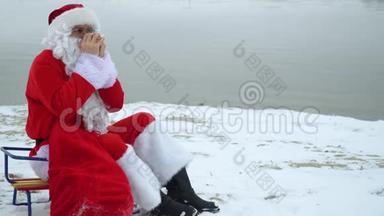 圣诞老人坐在湖的雪岸上，拿着一袋礼物<strong>喝</strong>着<strong>热水</strong>瓶里的咖啡