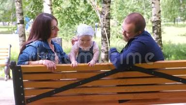 一家人爸爸妈妈和一个小女孩坐在城市公园的长椅上玩耍。