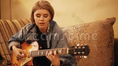 女孩弹吉他，在沙发上唱歌。 女人在室内创作音乐。 艺术家在吉他上表演。 一位音乐家