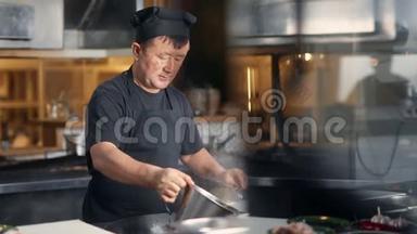 亚洲男厨师在煎锅上烹饪食物，在烹饪时加水。 中型摄影机