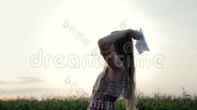 一位年轻女子在一片绿色的田野上举起一架纸飞机飞向蓝天，追随梦想的概念
