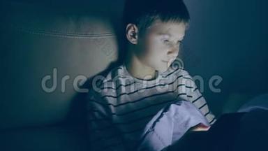 青少年男孩晚上在家使用平板电脑。 小男孩玩电脑游戏，看视频，上网冲浪