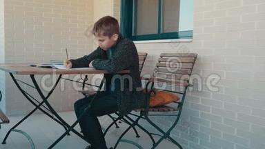 十几岁的男孩坐在户外露台上做学习任务。 学习，家庭作业，<strong>家庭教育</strong>，家庭隔离