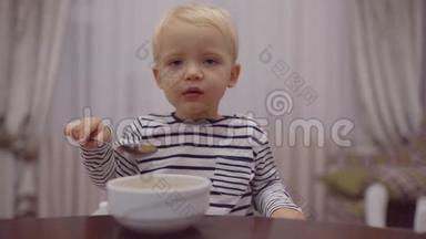快乐的婴儿用勺子吃食物。 笑开心萌娃在厨房吃水果捣碎.. 可爱的孩子