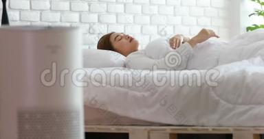 在舒适的白色卧室里，女人与空气<strong>净化器</strong>一起睡觉，用于过滤和清洁，去除灰尘，PM2.5，HEPA