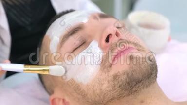 美容师正在用刷子`人脸上涂白色保湿面膜。