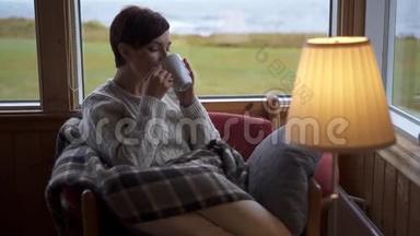 一个女人在家里的扶手椅上喝茶。