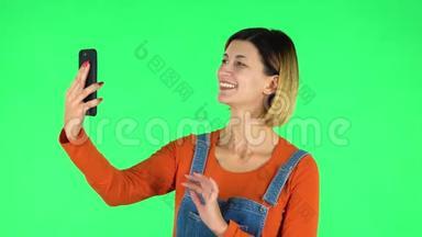 微笑的女孩用手机聊天视频。 绿色屏幕