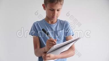 十几岁的男孩站着，手里拿着螺旋式学校作业本，笔记本，用钢笔写笔记