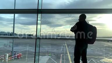 一位游客背着背包站在机场候机室明亮的大楼里，站在窗口看着<strong>街道</strong>，看着他的<strong>街道</strong>