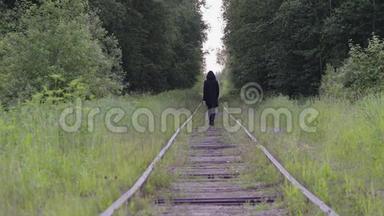 一个孤独的黑衣人走在树林里的铁轨上，后景。 他感到轻松、思考和无聊