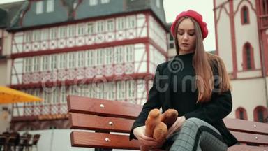 穿着黑色夹克的法国女人坐着，手里拿着裹着纸的长<strong>面包</strong>