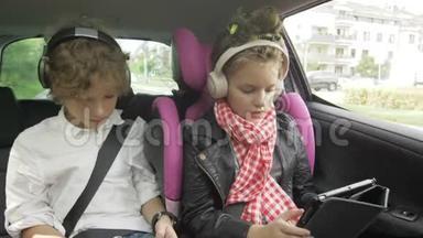 男孩和女孩带着耳机在汽<strong>车上</strong>玩平板电脑和智能手机，孩子们在汽<strong>车上</strong>使用设备。 兄弟和兄弟