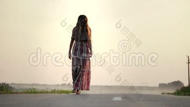 一个年轻漂亮的女孩穿着一件长裙子，在一个<strong>夏天</strong>温暖的<strong>夜晚</strong>赤脚走在路上