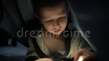 毯子下面的小家伙晚上在他的手机智能手机上玩游戏