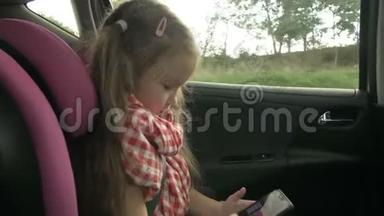 可爱的小女孩一边<strong>忙着</strong>用智能手机，一边坐在车的后座上。 可爱的小学儿童玩耍