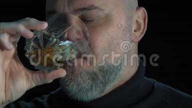 有感情的胡子男人喝威士忌加冰块。 孤立于黑色背景特写肖像。 酒精饮料和酒精