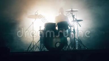 一个男人正在一个黑暗的工作室里用白烟打鼓。 鼓组，鼓包在黑暗中，鼓手演奏音乐会。